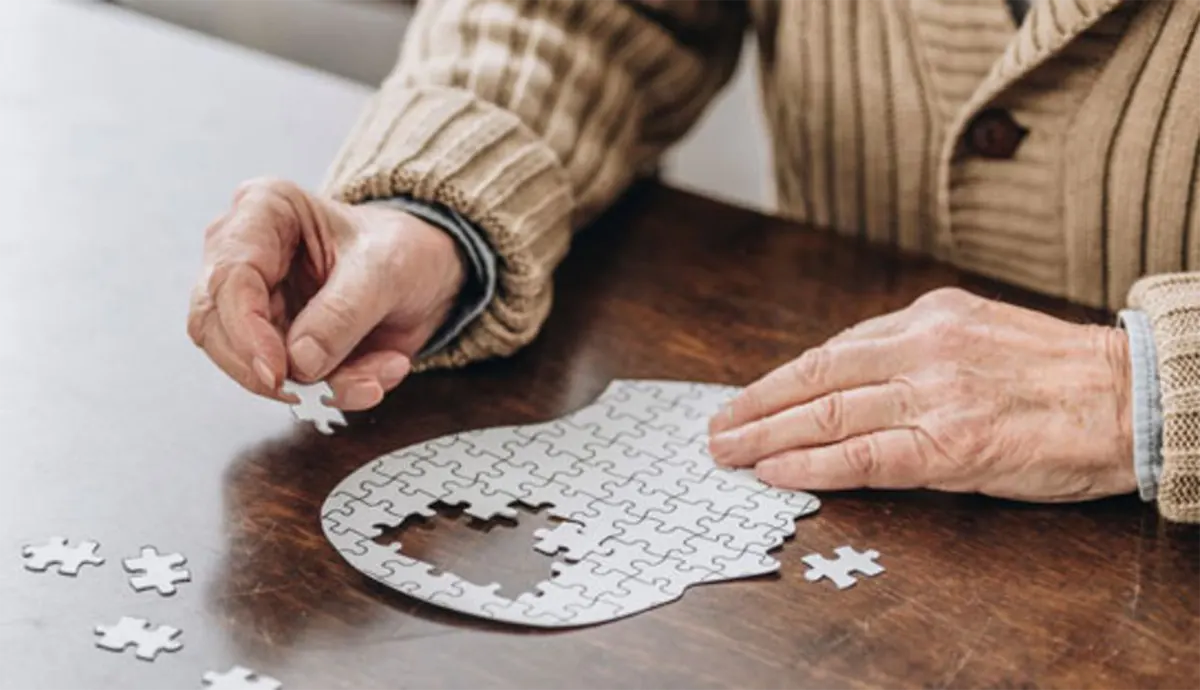 Na obrazku widać dłonie starszego mężczyzny, układającego puzzle