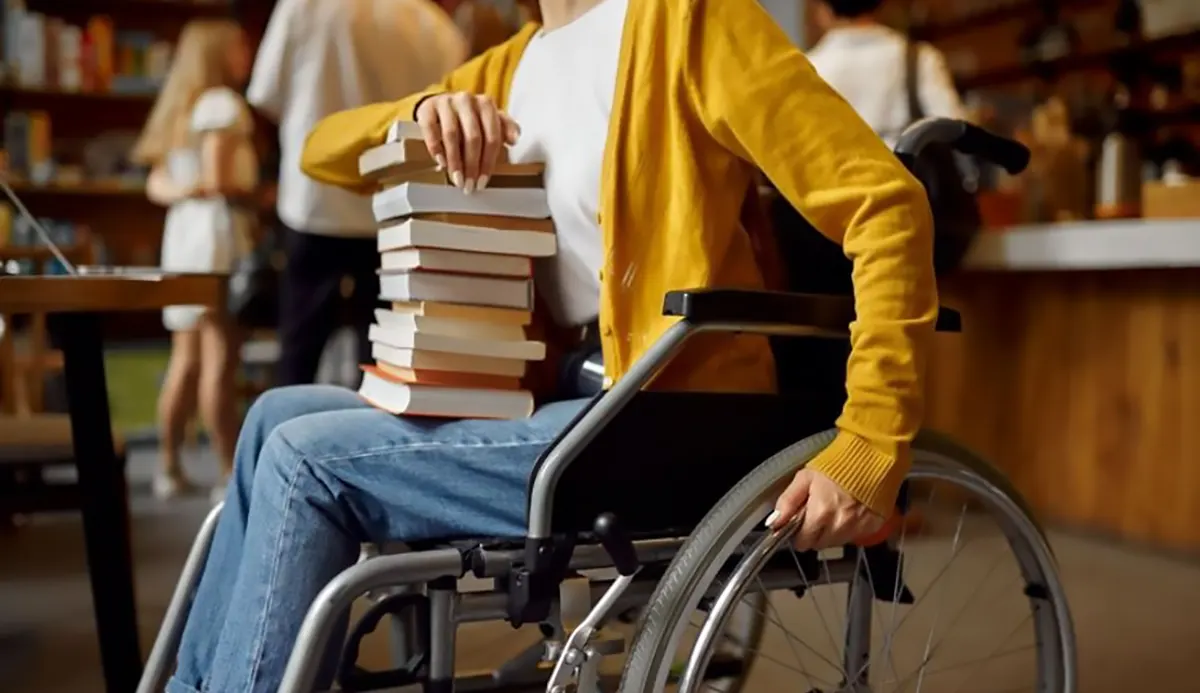 Kobieta na wózku, na kolanach ma stos książek